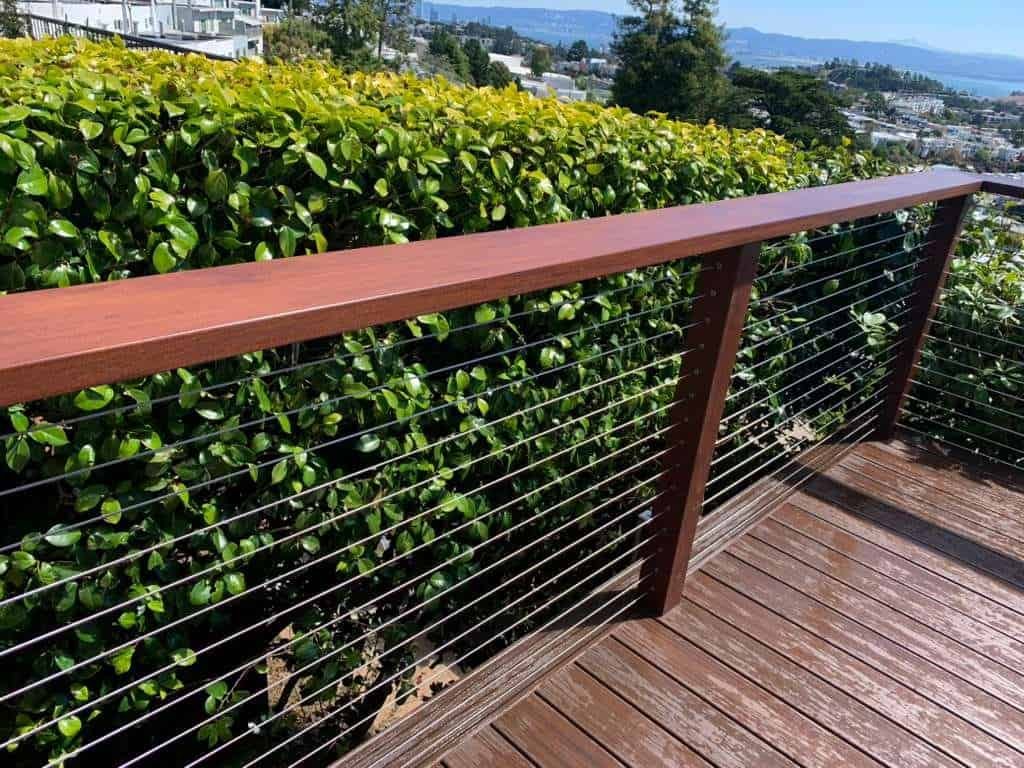 Outdoor wooden deck with cable railing, lush greenery, and scenic water view.